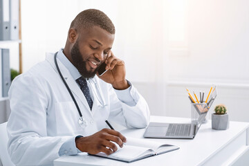 Young african doctor talking to patient on phone while working in modern clinic, high quality service concept