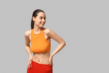 Beautiful young happy woman with piercing navel on grey background