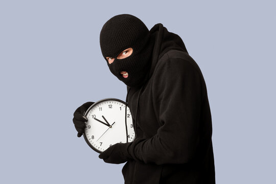 Portrait of sneaky robber wearing black balaclava and gloves holding clock, copy space, isolated over white studio wall