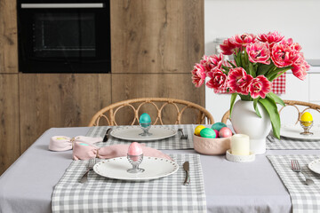 Vase with tulips, Easter eggs and dinnerware on dining table in kitchen