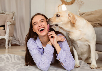 Animal Love Concept. Closeup of labrador retriever licking woman's cheek, lying on the floor in...