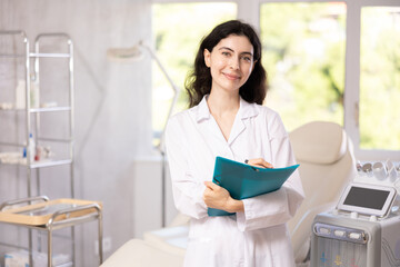 Female cosmetic doctor meticulously stands in her clinic, recording detailed notes in folder,...