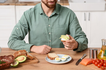 Man eating tasty toast with avocado and boiled eggs at wooden table