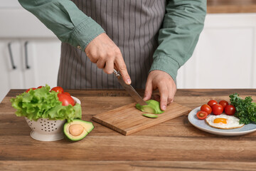 Man cutting fresh avocado for breakfast on wooden table