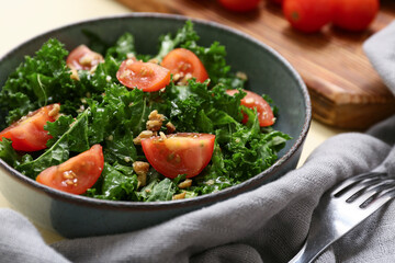 Bowl of tasty kale salad with tomatoes, napkin and fork, closeup