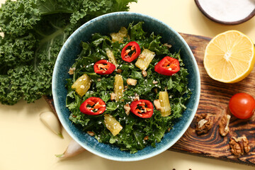 Bowl of tasty kale salad with orange, chili pepper and walnuts on color background