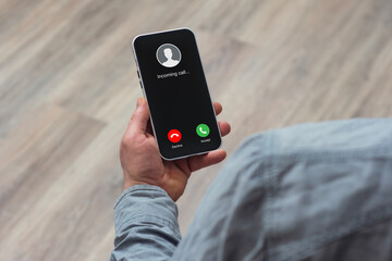 A man holds a smartphone in his hand with an incoming call against a wooden floor.