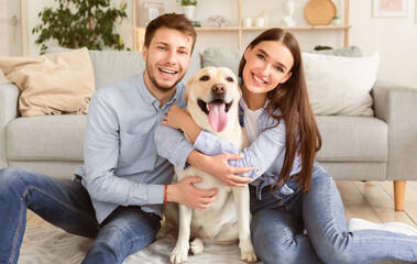 Bonding Concept. Beautiful young family embracing labrador sitting on the floor at their new home