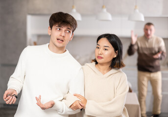 Adult man quarrels with couple of young guy and young woman in kitchen at home..