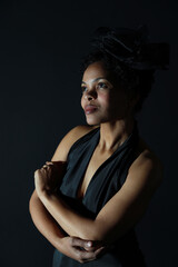 Fototapeta premium Low key portrait of young curly woman in black dress in shadows