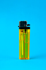 A transparent yellow plastic lighter standing upright against a bright blue background. The close-up shot highlights its metallic ignition mechanism and fluid inside, ideal for fire needs.