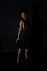 Full length low key portrait of slender curly woman in black dress