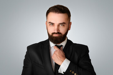 Handsome gentleman in business suit adjusting his tie against light grey background