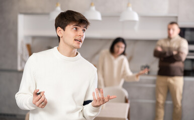 Fototapeta premium Adult man and young woman during family quarrel with young guy in kitchen
