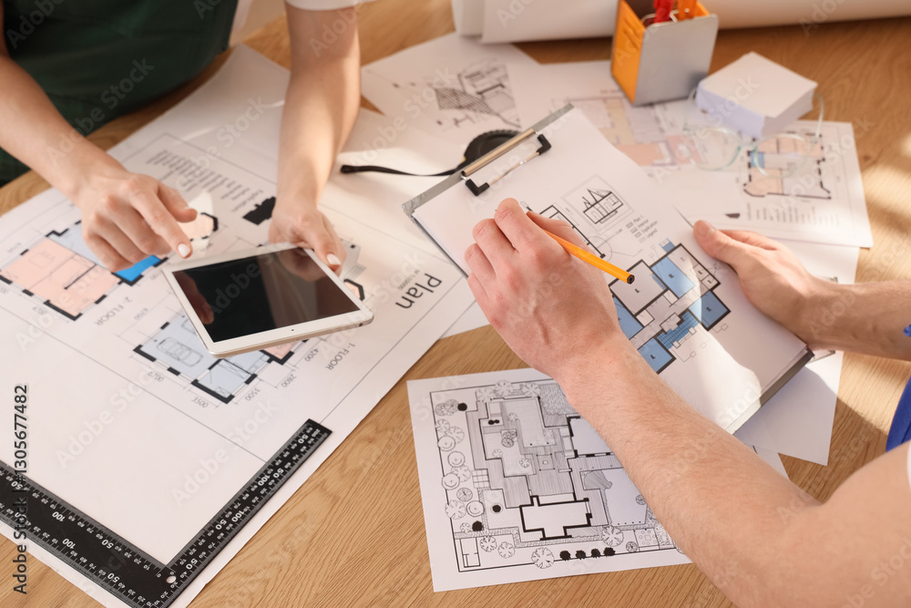 Poster constructors working with house plan and tablet computer at table in office, closeup