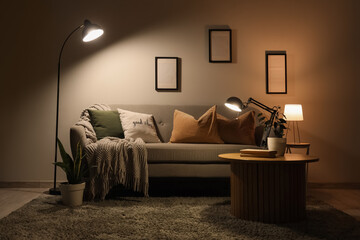 Interior of dark living room with sofa, table and glowing lamps in evening
