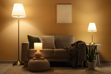 Interior of dark living room with sofa, pouf and glowing lamps in evening