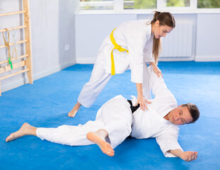 Coach teaches a young woman techniques for wrestling and throwing on sports mats during judo...