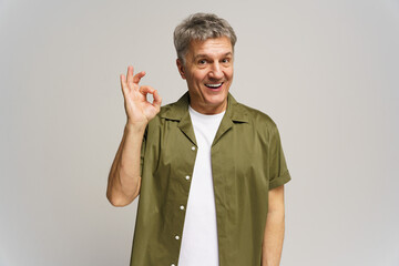Middle-aged man expresses positivity with hand gesture while smiling in studio setting