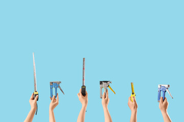 Many hands with construction staplers and measuring tapes on blue background