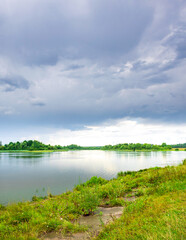 Cloudy sky over a lake with a green grassy area on the shore