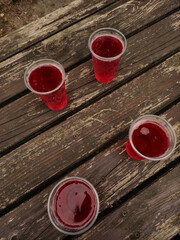 Four plastic cups with red drink Lemonade resting on weathered wooden table in kokorin, czechia