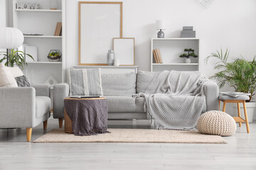 Interior of light living room with grey sofas, soft bench and shelf units