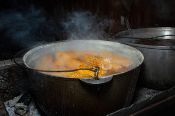 Corn heads boiled in a cauldron on a fire with smoke isolated on black background. Fast food....
