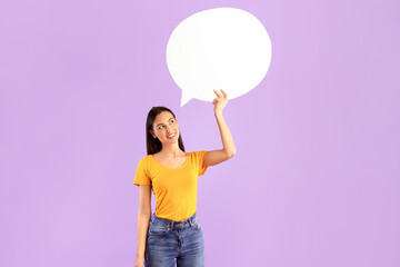 Good Idea Concept. Vertical portrait of pensive woman holding white blank speech bubble, thinking and looking up, empty space for announcement, isolated over purple studio background wall