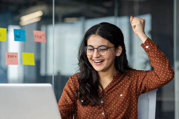 Successful woman at workplace inside office celebrating triumphant results of achievement....