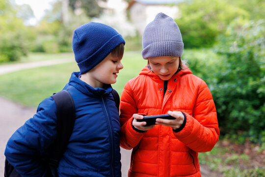 Portrait two happy smiling friends boys enjoy watching shorts video on social media at smartphone. Children enjoy playing game together sharing phone in school park outdoors