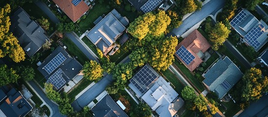 Aerial view of suburban neighborhood with solar panels on rooftops and lush green trees.