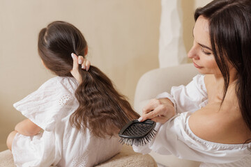 Mother brushing daughter's long hair in cozy home setting — family care, tenderness, and everyday...
