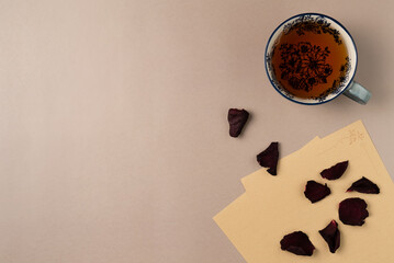 Cup of tea with vintage paper sheet with rose petals on beige background. Flat lay, top view. Copy space