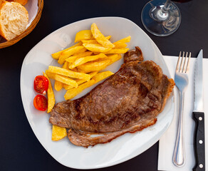 Deep-fried beef chop tenderloin is on round plate. Meat garnished with French fries and decorated with tomato, served with red wine
