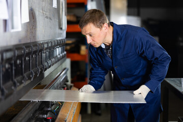 Focused professional craftsman in metalworking shop operating press brake, carefully positioning...