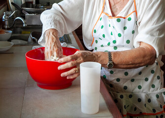 Elderly woman kneading dough in red bowl in kitchen