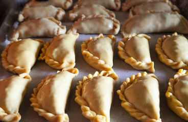 Delicious empanadas baking on parchment paper in oven tray