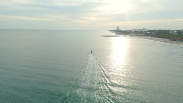 Aerial cinematographic view from a drone along the coast of Rio Hato with a boat sailing towards the sunset, on Farallon beach in the Panamanian Pacific from Panama, 4K vertical video.