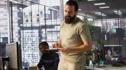 System administrator checking results on tablet after creating complex machine learning models that can process and analyze vast amounts of data. Admin standing in office, looking at device, camera A
