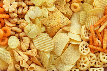 Colorful mix of salty snacks for beer varieties: chips and pretzels, onion rings and crackers. Non-healthy junk food background	