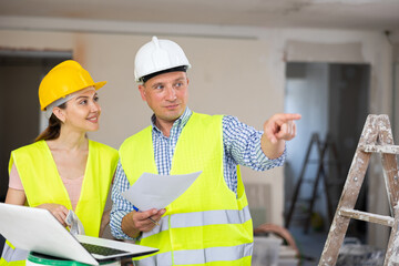 Fototapeta premium Portrait of woman architect and foreman holding blueprints discussing working process and gesturing in house being renovated