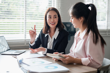 Two businesswomen engaged in a discussion over reports in a bright office environment, showcasing teamwork and collaboration.