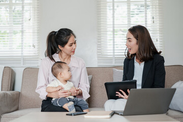 Businesswoman consulting a mother holding her baby in a modern living room, showcasing professional...