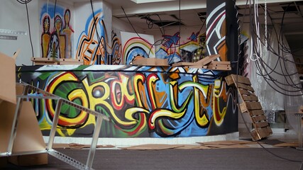 Empty abandoned warehouse with graffiti paintings on walls, concept of subversive culture, panning shot. City slums ghetto location used as crime haven by gang members doing street art