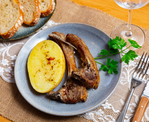 Roasted lamb ribs with potatoes served on plate with green parsley sprig.