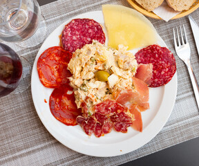 Appetizing Russian salad Olivier garnished with olive served with slices of Spanish sausages, cured jamon and cheese. Traditional tapa