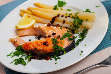 Baked fish salmon with garnish asparagus on a white ceramic plate in a restaurant