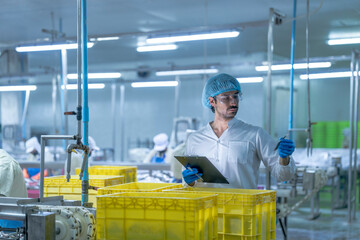 A supervisor in a food processing plant wearing protective gear, inspecting a fish while holding a...