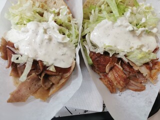 Close-up of two kebabs, one with beef and the other with chicken, topped with yogurt sauce and lettuce, wrapped in pita bread and served in paper bags, ready to eat.